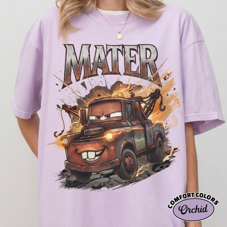 May include: A lilac t-shirt with a graphic of Mater from the film Cars. The word "MATER" is above the character. The design includes lightning bolts and a distressed look. The shirt is a Comfort Colors brand.