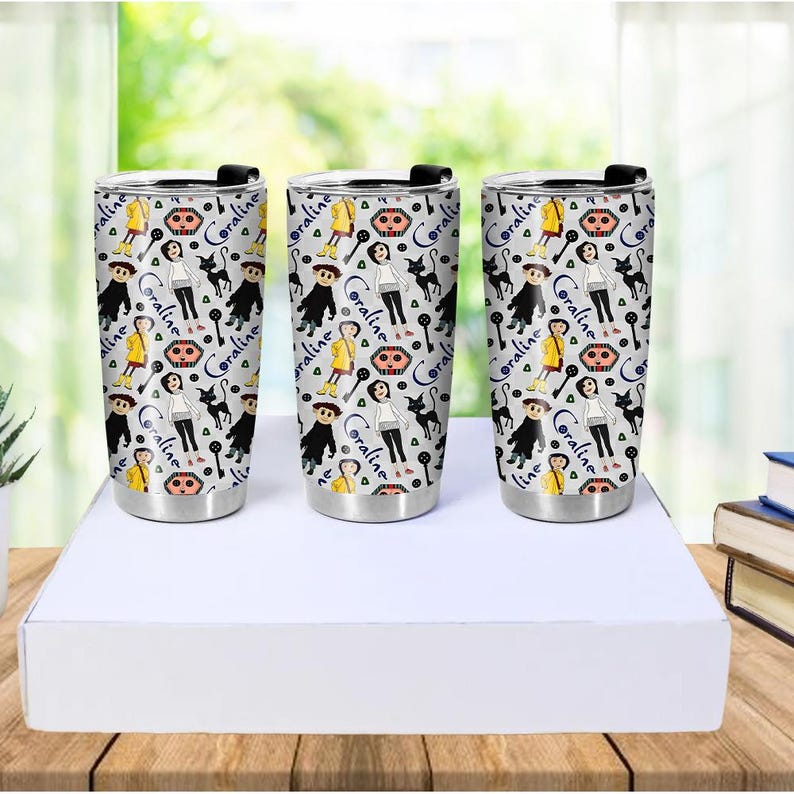 May include: Three stainless steel travel tumblers with a wraparound pattern featuring characters and elements from the movie "Coraline." The design includes illustrations of Coraline, the black cat, and other iconic imagery, set against a light gray background.