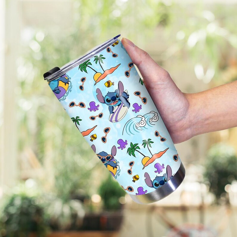 May include: A stainless steel tumbler featuring a light blue background with a repeating pattern of Stitch surfing, palm trees, sunglasses, and octopuses. The tumbler has a black lid and a silver base.