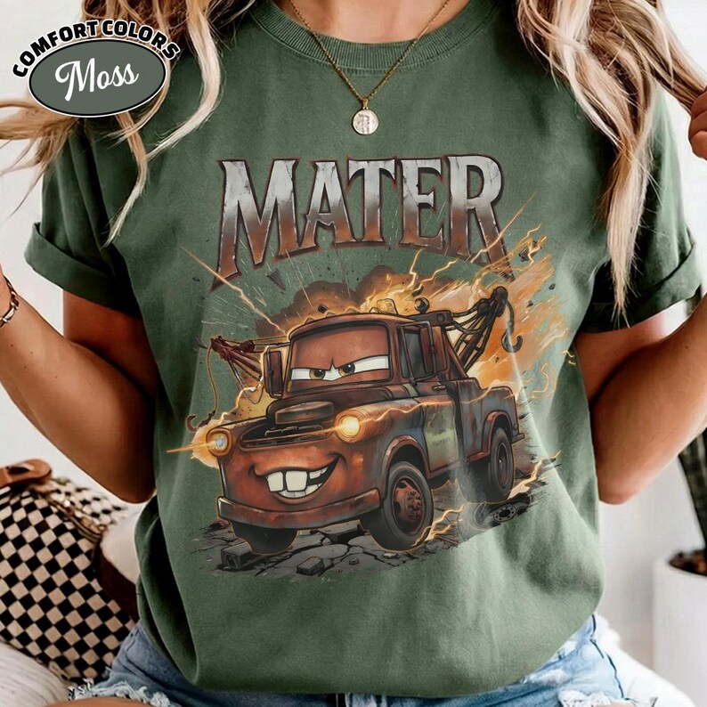 May include: Moss green Comfort Colors t-shirt with a graphic of Mater from the film Cars. The design features the name "MATER" in a distressed font above the cartoon tow truck, with lightning bolt accents.