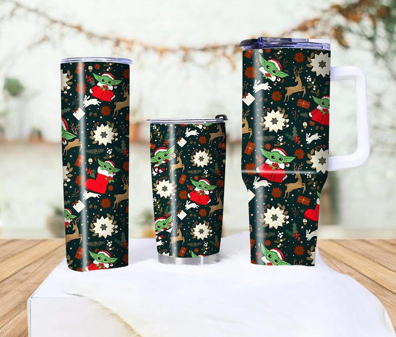 Pode incluir: Tr&ecirc;s canecas isoladas com um design festivo de Natal. As canecas apresentam um fundo verde escuro com um padr&atilde;o de Baby Yoda com roupa de Papai Noel, renas, flocos de neve e presentes. Uma caneca tem uma al&ccedil;a.