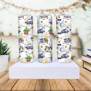 Op de afbeelding: Drie witte Star Wars-tumblers met een herhalend patroon van personages en schepen. Het ontwerp bevat Baby Yoda, BB-8 en de Millennium Falcon. De tumblers zijn cilindrisch en staan rechtop op een wit oppervlak.