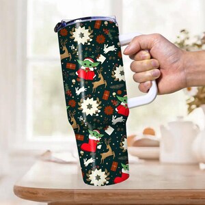 Pode incluir: Um copo grande e isolado com uma al&ccedil;a branca, com um padr&atilde;o festivo de Natal. O design inclui imagens de Baby Yoda, renas, estrelas e presentes em um fundo verde escuro. O copo foi projetado para manter as bebidas quentes ou frias.