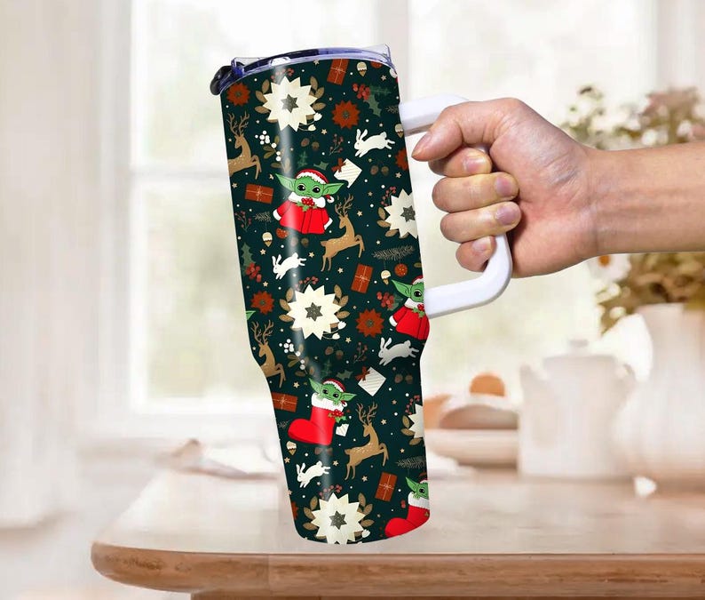 Pode incluir: Um copo grande e isolado com uma al&ccedil;a branca, com um padr&atilde;o festivo de Natal. O design inclui imagens de Baby Yoda, renas, estrelas e presentes em um fundo verde escuro. O copo foi projetado para manter as bebidas quentes ou frias.