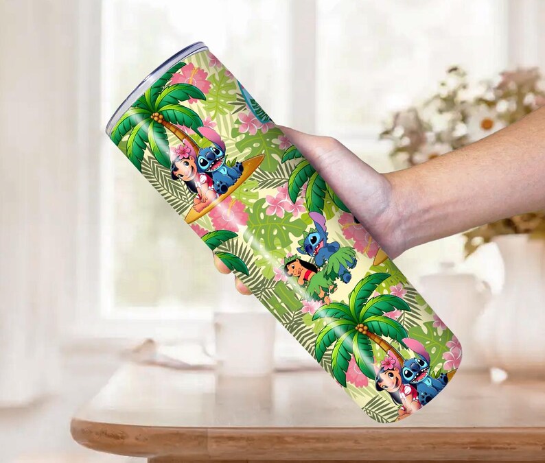 May include: A stainless steel tumbler featuring a tropical design with palm trees, pink flowers, and cartoon characters. The tumbler is cylindrical and has a silver rim. The design includes the characters Stitch and Lilo.