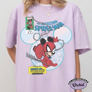 May include: A light purple t-shirt featuring a Marvel comic book-style graphic of Mickey Mouse as Spider-Man. The design includes the text "The Amazing Spider-Man" and "What If... Mickey Mouse Was Bitten By A Radioactive Spider?"
