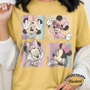 May include: Mustard yellow t-shirt featuring four panels with Minnie Mouse illustrations. Each panel shows Minnie in different poses, wearing a pink bow and various outfits. The shirt has the words "COMFORT COLORS" and "Mustard" printed on it.