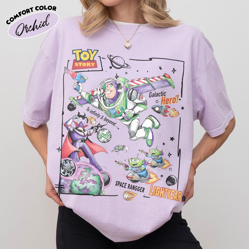 May include: A light purple t-shirt featuring a graphic print of Buzz Lightyear, Zurg, and aliens from Toy Story. The design includes the text TOY STORY, To infinity & beyond, Galactic Hero, SPACE RANGGER, and LIGHTYEAR with space-themed illustrations.
