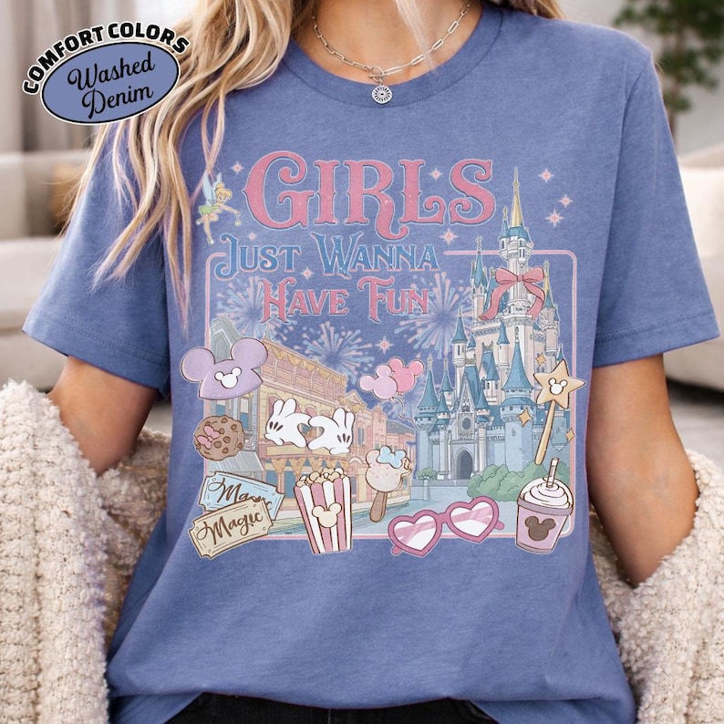 May include: Blue Comfort Colors t-shirt with the text "Girls Just Wanna Have Fun" in pink. The graphic includes a castle, fireworks, and cartoon food items. The shirt has a washed denim look.