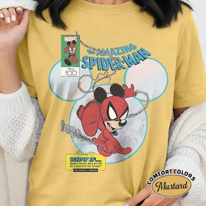 May include: Mustard-colored t-shirt featuring a comic-style illustration of Mickey Mouse as Spider-Man. The design includes the text "The Amazing Spider-Man," "Marvel," and "Disney 100." The shirt also has the text "What If... Mickey Mouse Was Bitten by a Radioactive Spider?"