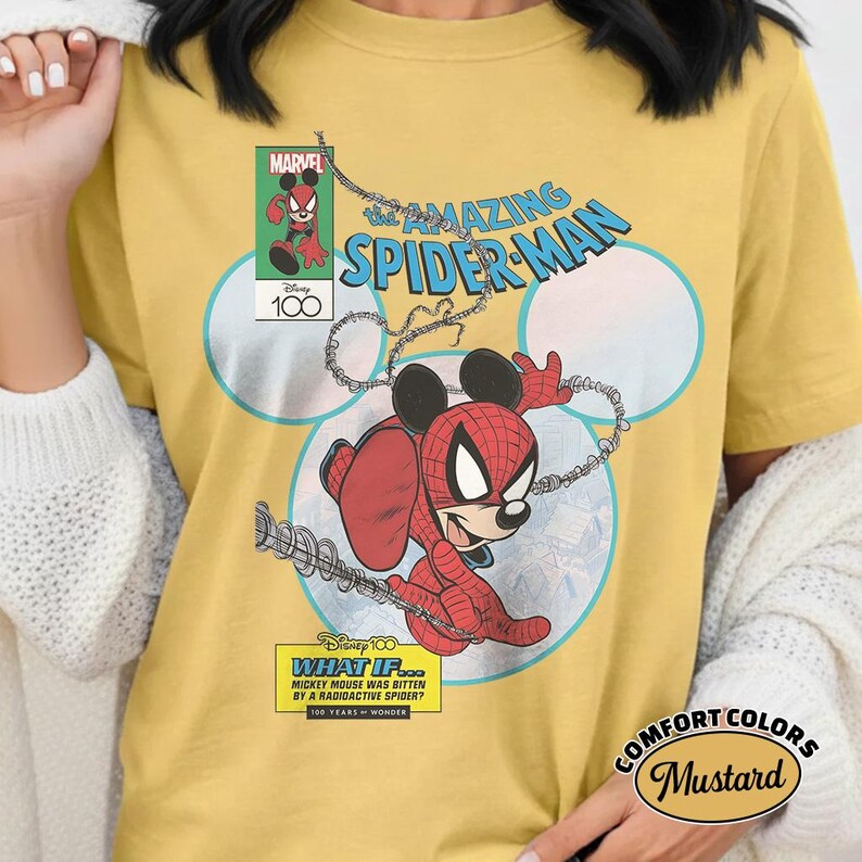 May include: Mustard-colored t-shirt featuring a comic-style illustration of Mickey Mouse as Spider-Man. The design includes the text "The Amazing Spider-Man," "Marvel," and "Disney 100." The shirt also has the text "What If... Mickey Mouse Was Bitten by a Radioactive Spider?"
