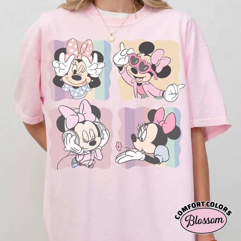 May include: Pink t-shirt featuring four panels with Minnie Mouse illustrations. Each panel shows Minnie in different poses, wearing a bow and various outfits. The shirt has a Comfort Colors Blossom label.