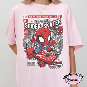 Puede incluir: Camiseta rosa claro con un gr&aacute;fico de c&oacute;mic de Spider-Man en monopat&iacute;n. El dise&ntilde;o incluye el texto "THE AMAZING SPIDER SKATER" y "WITH GREAT POWER COMES GREAT RESPONSIBILITY". La camiseta es de Comfort Colors.