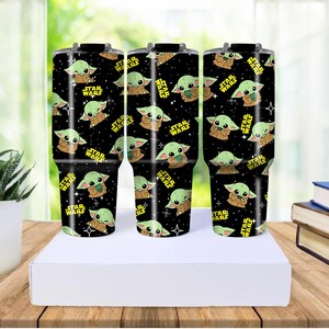 May include: Three black insulated travel mugs with a repeating pattern of a green alien character and the text "STAR WARS" in yellow. The mugs are displayed on a white surface.