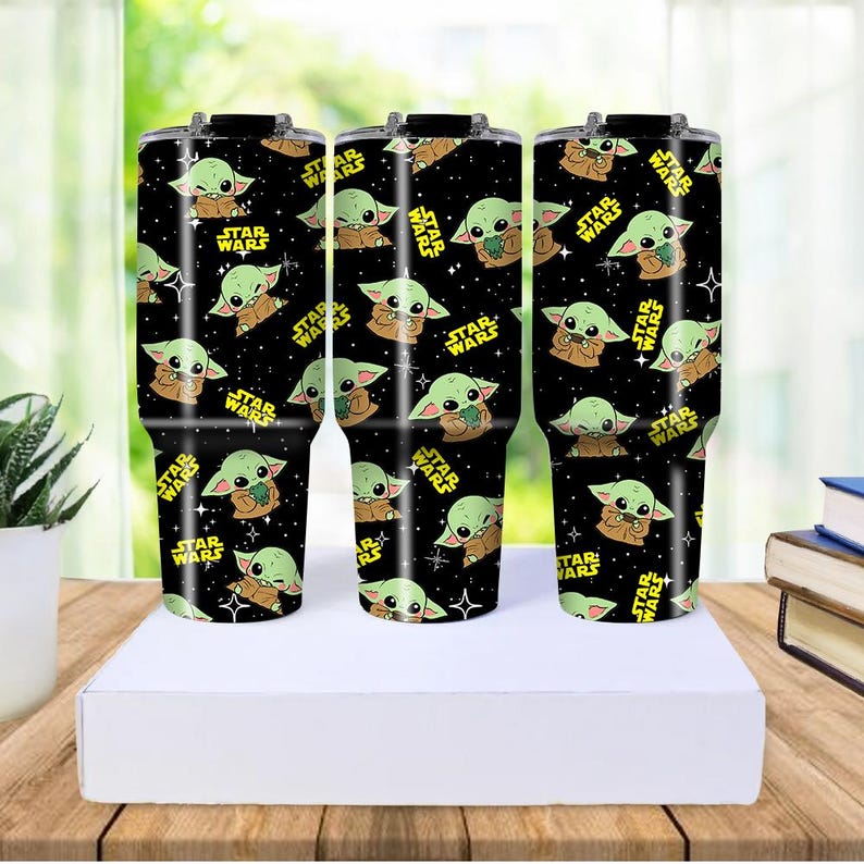 May include: Three black insulated travel mugs with a repeating pattern of a green alien character and the text "STAR WARS" in yellow. The mugs are displayed on a white surface.