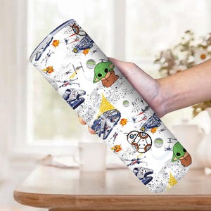 Op de afbeelding: Een witte beker met een herhaald patroon van Star Wars-personages en ruimtevaartuigen. Het ontwerp bevat afbeeldingen van Baby Yoda, ruimteschepen en andere iconische elementen uit de franchise. De beker wordt door een persoon vastgehouden.