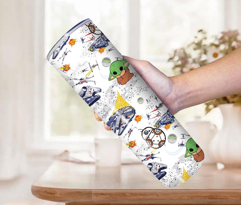 Op de afbeelding: Een witte beker met een herhaald patroon van Star Wars-personages en ruimtevaartuigen. Het ontwerp bevat afbeeldingen van Baby Yoda, ruimteschepen en andere iconische elementen uit de franchise. De beker wordt door een persoon vastgehouden.
