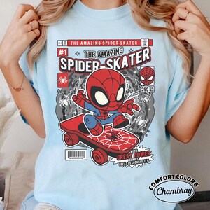 Puede incluir: Camiseta azul claro con un dise&ntilde;o de c&oacute;mic de Spider-Man en monopat&iacute;n. El dise&ntilde;o incluye el texto "The Amazing Spider Skater" y "Great Power Comes Great Responsibility."