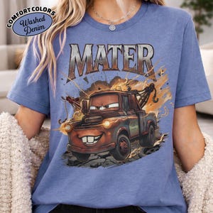 May include: A blue t-shirt with a graphic of Mater from the Cars film. The design includes the word "MATER" above the character, with lightning and fire effects. The shirt has "COMFORT COLORS" and "Washed Denim" text.