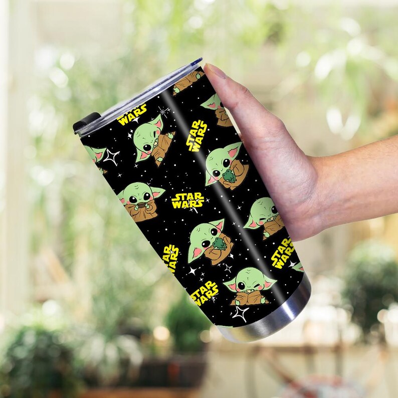 May include: A stainless steel travel mug with a black background and a repeating pattern of Grogu from Star Wars. The words "STAR WARS" are in yellow. The mug has a black lid.