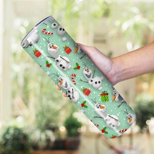 Puede incluir: Un vaso cil&iacute;ndrico con un dise&ntilde;o festivo que presenta al personaje Olaf de la pel&iacute;cula Frozen. El vaso tiene un fondo verde claro con patrones repetidos de Olaf, bastones de caramelo, regalos y acebo. El vaso est&aacute; sostenido en una mano.