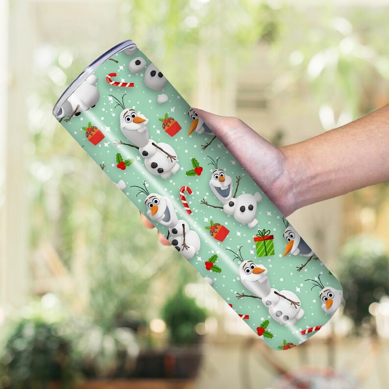 Puede incluir: Un vaso cil&iacute;ndrico con un dise&ntilde;o festivo que presenta al personaje Olaf de la pel&iacute;cula Frozen. El vaso tiene un fondo verde claro con patrones repetidos de Olaf, bastones de caramelo, regalos y acebo. El vaso est&aacute; sostenido en una mano.