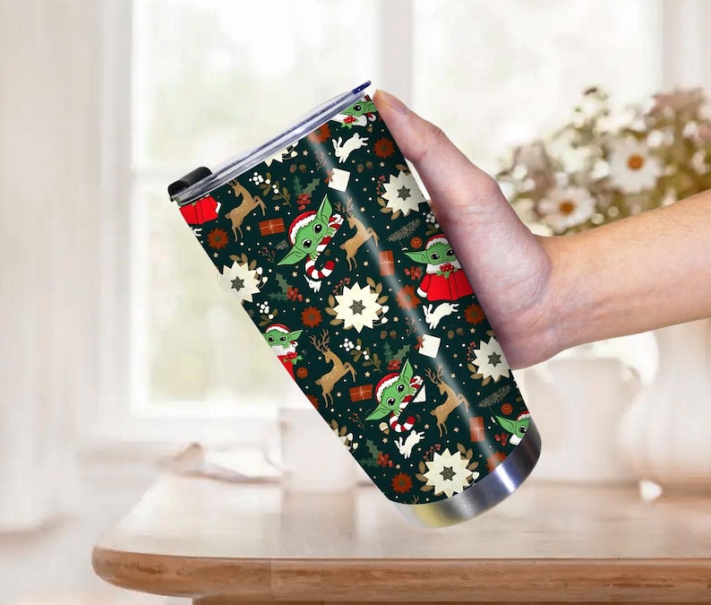 Pode incluir: Um copo de a&ccedil;o inoxid&aacute;vel com um design de Natal festivo. O copo apresenta um fundo verde escuro com padr&otilde;es repetidos de um personagem alien&iacute;gena verde, renas, flocos de neve e presentes. O personagem est&aacute; usando um chap&eacute;u de Papai Noel e roupas vermelhas.
