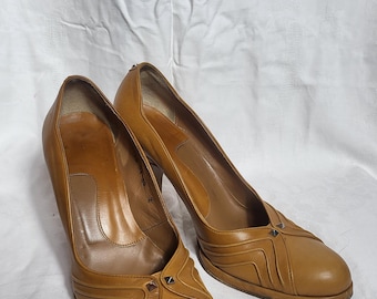 May include: A pair of tan leather court shoes with a pointed toe and a high heel. The shoes feature decorative stitching and small silver studs on the vamp. The shoes are set against a white background.