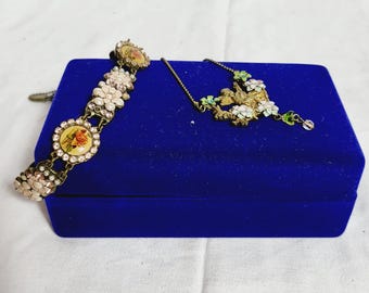Puede incluir: Un conjunto de joyas vintage con pulsera y collar. La pulsera tiene detalles florales y ovalados con un acabado dorado. El collar tiene un diseño floral a juego. Ambas piezas se exhiben en una caja de terciopelo azul.