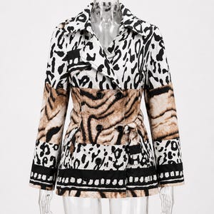 May include: A double-breasted jacket featuring a mix of animal print patterns in black, white, and tan. The garment has a notched collar, long sleeves, and a tie-waist belt. The lower section includes a horizontal black and white striped border.