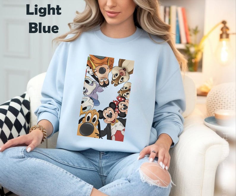 May include: Light blue sweatshirt featuring a rectangular graphic of various cartoon characters, including Mickey and Minnie Mouse, Goofy, and Pluto. The text "Light Blue" is in the upper left corner. The sweatshirt is worn by a person.
