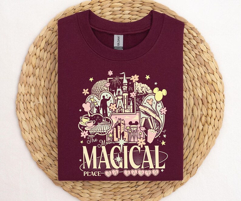Może przedstawiać: Bordowa bluza z kolorową grafiką przedstawiającą zamek, Myszka Miki i napis "The Most Magical Place on Earth". Bluza wykonana jest z miękkiego materiału.