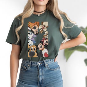 May include: Dark green t-shirt featuring a graphic of Disney characters, including Mickey Mouse, Minnie Mouse, and Pluto. The characters are arranged in a semi-circle. The shirt is made of a soft material.