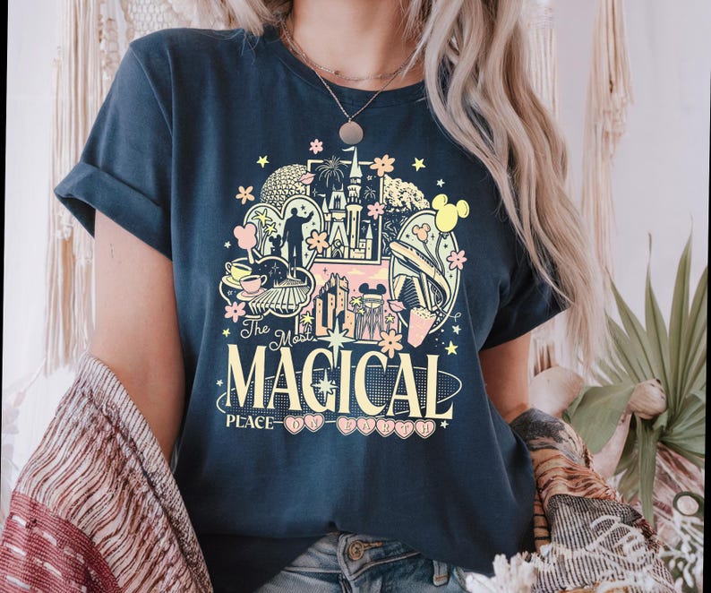 Może przedstawiać: Granatowa koszulka z kolorową grafiką przedstawiającą zamek, Myszka Miki i napis "The Most Magical Place". Projekt zawiera pastelowe r&oacute;żowe, ż&oacute;łte i niebieskie elementy. Koszulka ma podwinięte rękawy.
