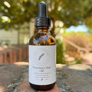 May include: A brown glass bottle of Rosemary Hair Oil with a black dropper. The label reads "RO & LAVENDER" and "Rosemary Hair Oil". The bottle is 2 fl. oz. (59 ml).