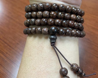 May include: A stack of dark brown wooden bead bracelets. The beads have a natural wood grain pattern. The bracelets are wrapped around a wrist, with a dark brown string and additional beads hanging down.