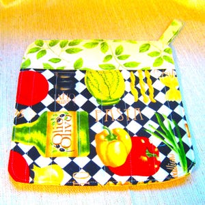 May include: A quilted pot holder with a black and white checkered pattern, featuring images of pasta, vegetables, and olive oil. The top border has a green leaf design. The word "PASTA" is printed on the pot holder.