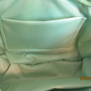 May include: Interior view of a light green tote bag with a matching pocket. The bag's interior is a solid, pale green, and the pocket is rectangular. The bag's exterior is a lighter green with a textured pattern.