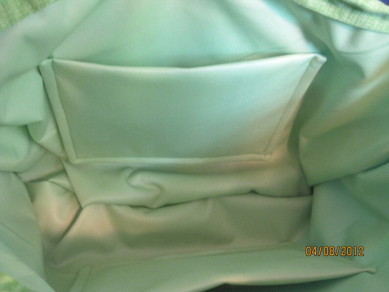 May include: Interior view of a light green tote bag with a matching pocket. The bag's interior is a solid, pale green, and the pocket is rectangular. The bag's exterior is a lighter green with a textured pattern.