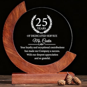 Puede incluir: Un premio de madera y vidrio con el texto "25 AÑOS DE SERVICIO DEDICADO Ms. Carter". El premio tiene una base de madera oscura y un marco de madera curvado. El texto es blanco sobre fondo negro.