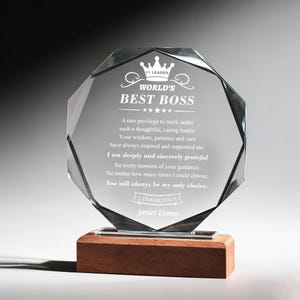 May include: A clear, multi-faceted glass award with the words "WORLD'S BEST BOSS" and a crown design. The award is mounted on a rectangular wooden base. The text includes a message of thanks and the name "Javier Limon".