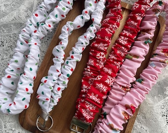 Puede incluir: Una colección de cordones de tela con varios diseños festivos, incluyendo rojo con copos de nieve blancos, blanco con lunares rojos y verdes, y rosa con hombres de jengibre. Cada cordón tiene un cierre de metal plateado.