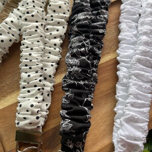 May include: Three fabric lanyards with silver-tone metal hardware and key rings. One is white with black polka dots, one is black with a white floral line-art pattern, and one is solid white with a textured, eyelet-style fabric finish.