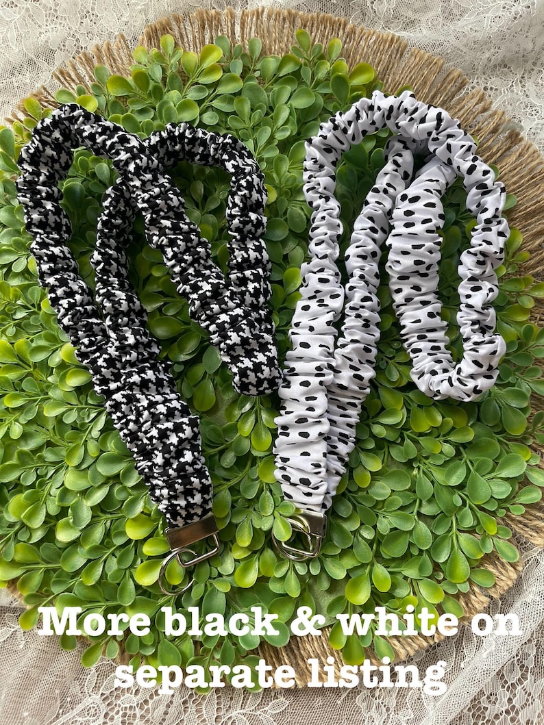 May include: Two fabric lanyards with metal hardware. One lanyard features a black and white houndstooth pattern, while the other has a white fabric with black spots. Both are gathered and ruffled along the length of the strap.