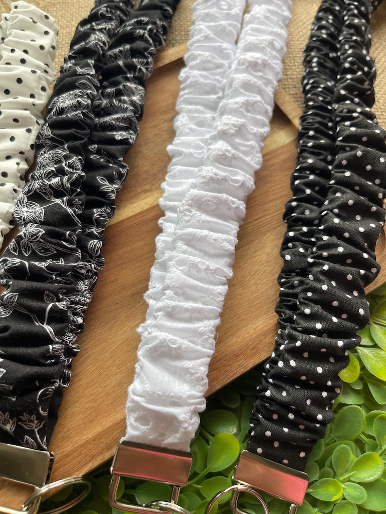 May include: Four fabric lanyards with silver-tone metal hardware and key rings. The collection includes a white lanyard with black polka dots, a black lanyard with a white floral pattern, a solid white eyelet lanyard, and a black lanyard with white dots.