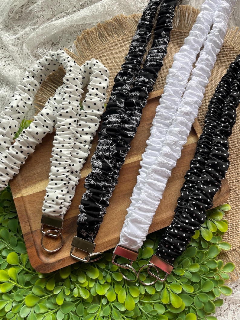 May include: Four fabric lanyards with gathered, scrunchie-style designs. One is white with black polka dots, one is black with white floral patterns, one is solid white with a textured surface, and one is black with small white polka dots.