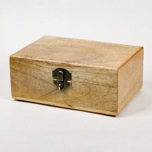May include: A rectangular wooden box with a hinged lid and a metal clasp. The box is made of light-colored wood with visible grain and a natural finish. The metal clasp is a dark bronze color.