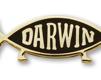 May include: A gold-colored pin in the shape of a fish, with the word "DARWIN" in bold, white letters on a black background. The pin has a shiny, metallic finish and is likely a lapel pin or badge.