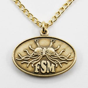 May include: Gold-toned necklace featuring an oval pendant with a stylized depiction of the Flying Spaghetti Monster, with the letters "FSM" below. The necklace has a gold chain.