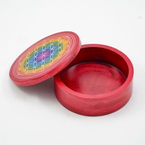 Op de afbeelding: Een ronde, rode houten doos met een deksel. Het deksel is open en onthult de binnenkant van de doos. Het deksel heeft een kleurrijk regenboogontwerp. De doos is gemaakt van hout en heeft een gladde afwerking.